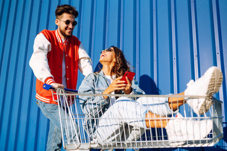 Stylish man and woman having fun and riding shopping cart. Lifestyle, leisure, entertainment, youth.の写真素材