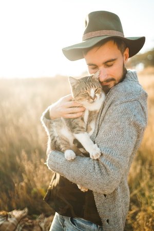 Lovely young hipster with a cat. A guy with a mustache and a beautiful smile is hugging a cat.の写真素材