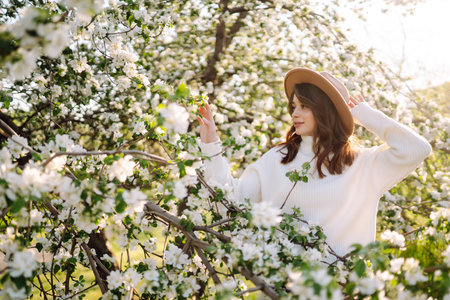 Portrait of Beautiful Woman In hat posing near flowering. Smiling woman enjoying the smell of flowers.の写真素材
