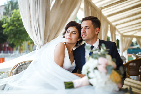 Young bride and groom in a cafe. Husband and wife hold each other's hands. Loving couple in a restaurant.の写真素材