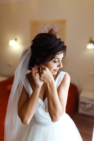 Morning of the bride. Beautiful smiling brunette bride in a white dress with a wedding bouquet in her hands.の写真素材