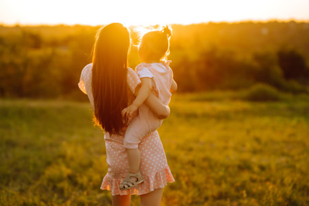 Mother and little daughter playing together in summer sunset. Happy mom with small child having fun.の写真素材