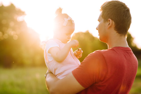 Happy dad and little baby girl having fun in summer park at sunset. Dad plays with small child.の写真素材