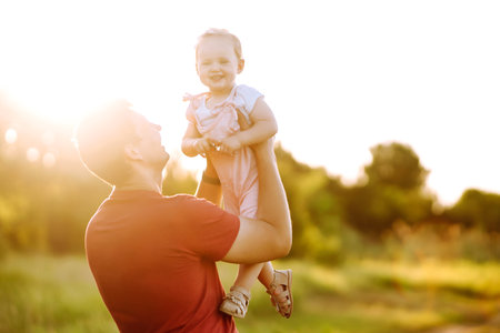 Happy dad and little baby girl having fun in summer park at sunset. Dad plays with small child.の写真素材