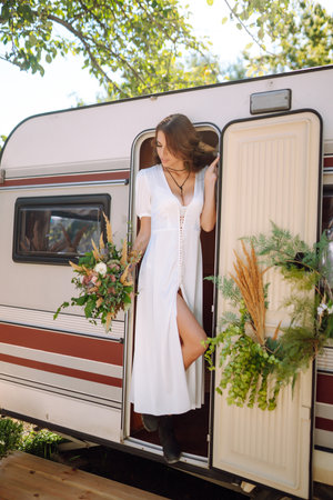 Beautiful stylish bride near trailer. camping season. Marriage. happy newlywed woman.の写真素材