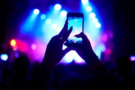 Hand with a phone records live music festival. People taking photographs with smart phone during concert.の写真素材