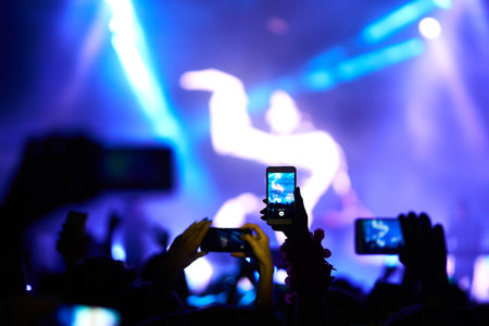 Hand with a phone records live music festival. People taking photographs with smart phone during...