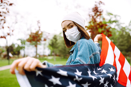 Girl in protective sterile medical mask and with american flag in hand.の写真素材