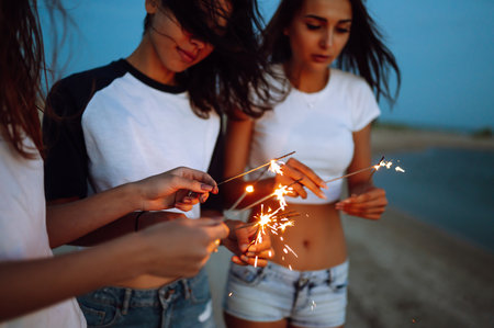 The sparklers in the hands of young girls on the beach. Three girls enjoying party on beach with sparklers.の写真素材