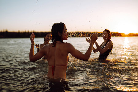 Three young girls splashing water in the sea. Happy friends having fun in the waves at sunset time.の写真素材