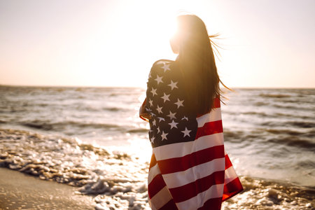 View from the back young brunette female person holding national American flag.の写真素材