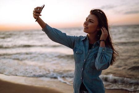 Beautiful girl takes a selfie on the beach at sunset. The concept of relax, travel and summer vacation.の写真素材