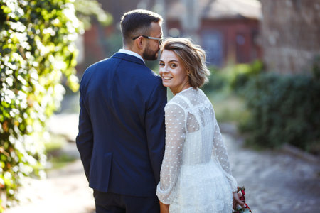 Couple enjoying romantic moments while walking in the park. Stylish bride and groom posing and kissing.の写真素材