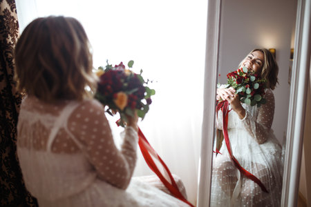Bride in elegant white dress looking in the mirror. The bride smiles and poses in front of the mirror.の写真素材