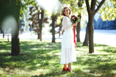 Beautiful bride with wedding bouquet in the park. Elegant woman with professional make up and hair styleの写真素材