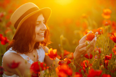 Beautiful girl in the poppy field at sunset in a white dress and hat.の写真素材