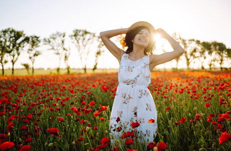 Beautiful girl in the poppy field at sunset in a white dress and hat.の写真素材