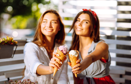 Ice cream in the hands of beautiful young girls. Two female friends eat ice cream walking in the park.の写真素材