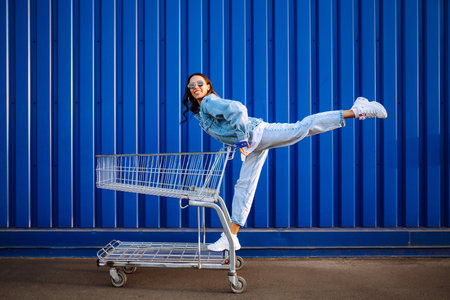 Young woman with shopping cart having fun near color wall. smiling african woman going shopping.の写真素材