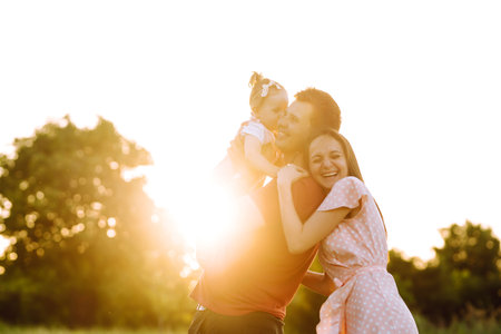 Happy young family walking in the park at sunset. Mom, dad and little daughter having fun in the park.の写真素材