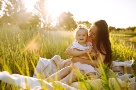 Mother and daughter playing together in summer park at sunset. happy mom with small child having funの写真素材