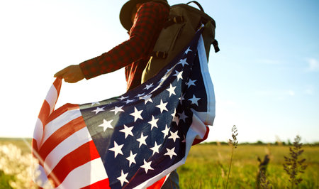 4th of July. american flag. Traveler with the flag of America. The man in a hat, a backpack, a shirt and jeans.の写真素材