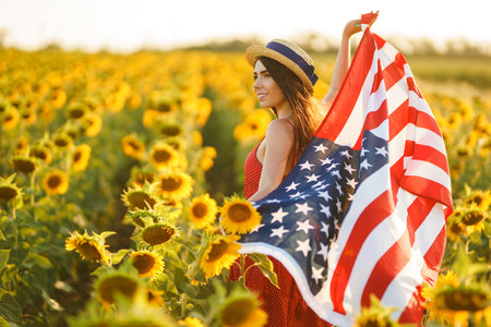 Beautiful girl in hat with the American flag in a sunflower field. 4th of July. Fourth of July. Freedomの写真素材
