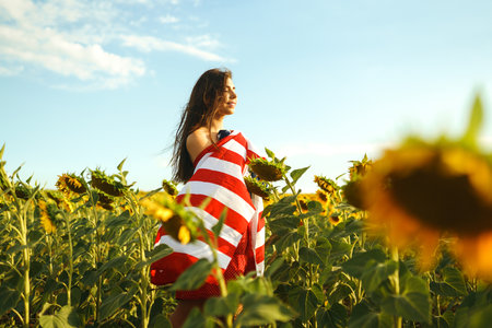 Beautiful girl in hat with the American flag in a sunflower field. 4th of July. Fourth of July. Freedomの写真素材