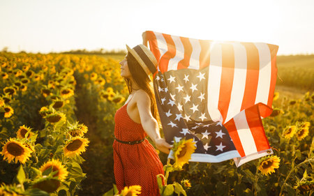 Beautiful girl in hat with the American flag in a sunflower field. 4th of July. Fourth of July. independence day.の写真素材