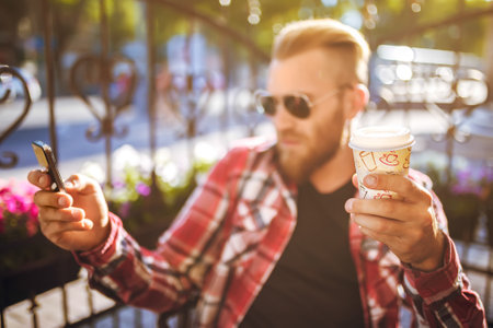 Handsome young man holding mobile phone and drinking coffee while sitting in the rest area.の写真素材