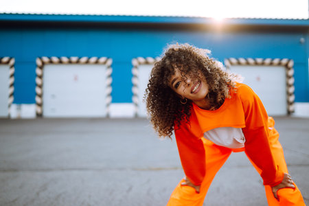Young African American woman - dancer dancing in the street at sunset. Stylish woman with curly hair in an orange suit showing some moves.の写真素材