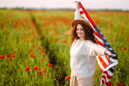 Young woman holding waving american USA flag in the poppy field. Independence Day, 4th July.の写真素材