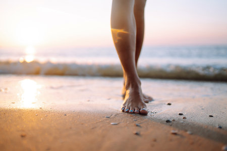 Close- up leg of young woman walking along wave of sea water and sand on the summer beach.の写真素材