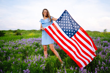Young woman with american USA flag on blooming meadow. Independence Day, 4th July.