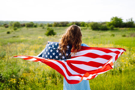 Young woman with american USA flag on blooming meadow. Independence Day, 4th July.
