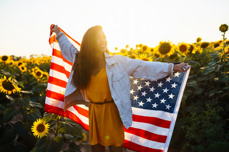 Woman proudly hold waving american USA flag in the sunflower field. Independence Day, 4th July.の写真素材