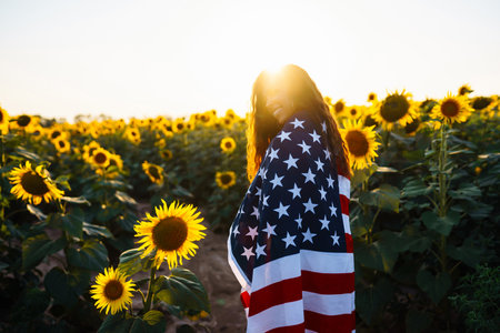 Woman proudly hold waving american USA flag in the sunflower field. Independence Day, 4th July.の写真素材