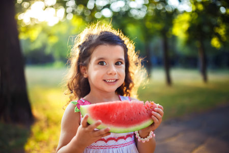 Funny kid eating watermelon outdoors in summer park, focus on eyes. Child, healthy food. Youth lifestyle.の写真素材