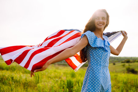 Young woman proudly hold waving american USA flag on blooming meadow. 4th of July. independence day.の写真素材