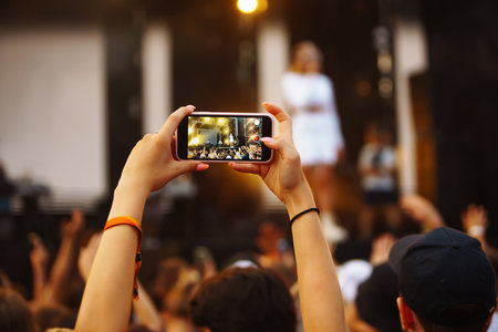Hand with a phone records live music festival. People taking photographs with smart phones.