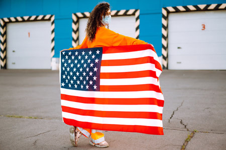 African American woman with medical face mask posing with american flag.The concept of preventing the spread of the epidemic. Covid-2019.の写真素材