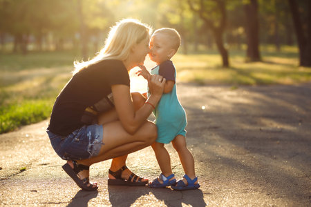 Kiss and hugs of mom and son. Mom and son walk in the summer park. Family holiday and togetherness.の写真素材