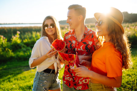 Friends eating watermelon on picnic. People enjoy summer time. People, travel, holidays concept.の写真素材