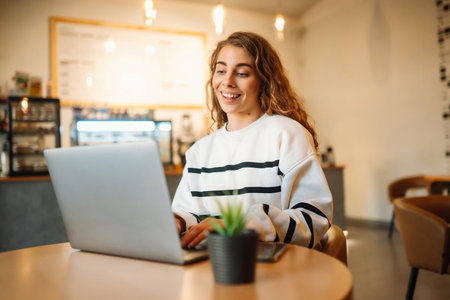 Young woman sits in a cafe and works on computer. Business, blogging, freelance, education concept.の写真素材