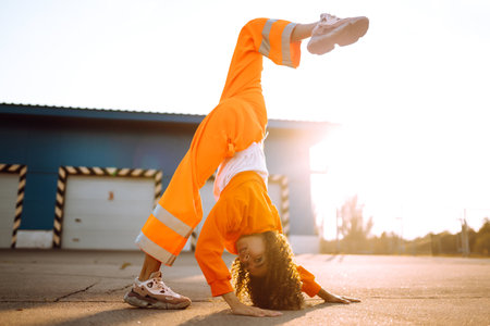 Young African American woman - dancer dancing in the street at sunset. Stylish woman with curly hair in an orange suit showing some moves.の写真素材