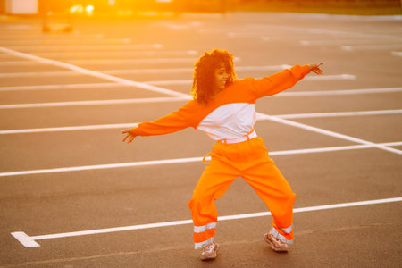 Young African American woman - dancer dancing in the street at sunset. Stylish woman with curly hair in an orange suit showing some moves.の写真素材
