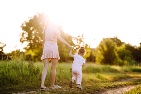 Mother and daughter playing together in summer park at sunset. happy mom with small child having funの写真素材