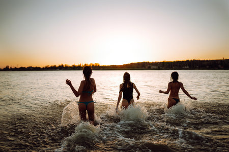 Young girls run to the sea at sunset. Beach holiday and summer vacation concept.の写真素材
