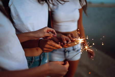 The sparklers in the hands of young girls on the beach. Three girls enjoying party on beach with sparklers.の写真素材