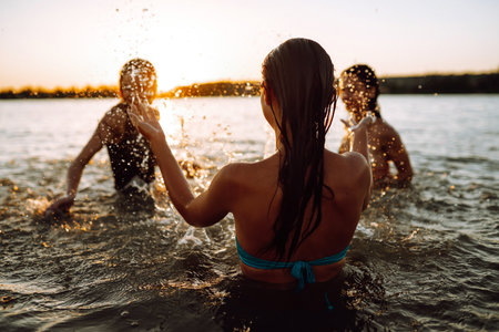 Three young girls splashing water in the sea. Happy friends having fun in the waves at sunset time.の写真素材